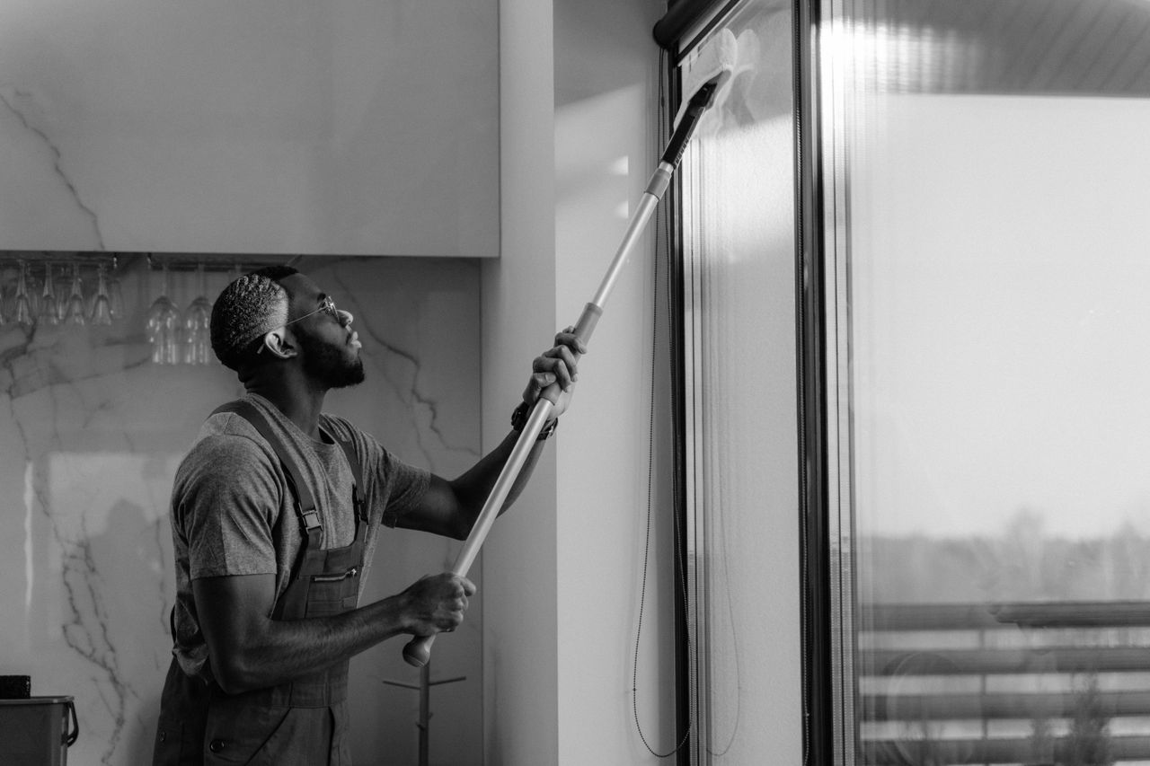 Un homme nettoie une vitre avec un balai à vitre en noir et blanc, illustrant un travail professionnel.
